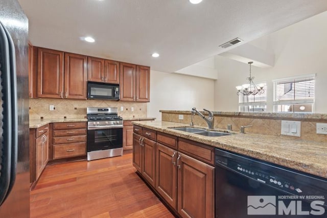 kitchen featuring visible vents, light stone counters, wood finished floors, black appliances, and a sink