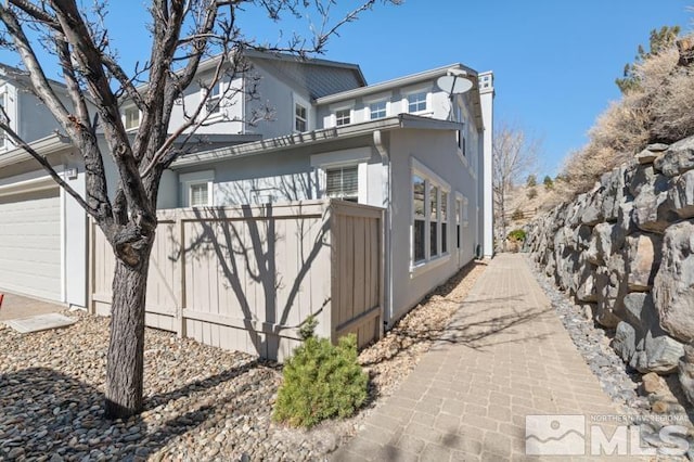 view of side of home featuring a garage, fence, and stucco siding