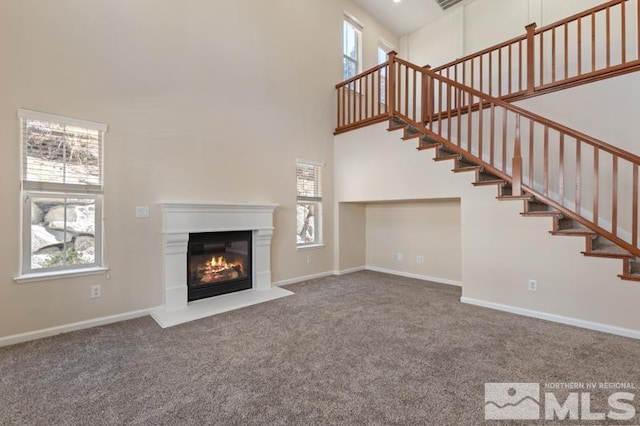 unfurnished living room with stairs, carpet floors, a glass covered fireplace, and a towering ceiling