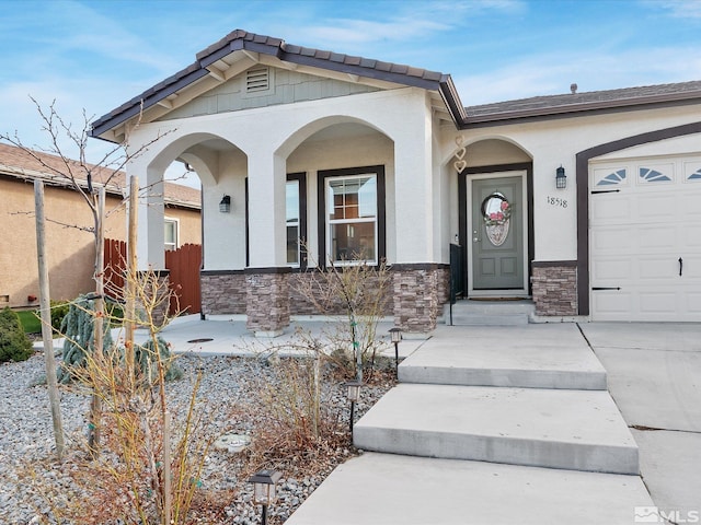 entrance to property featuring an attached garage, stone siding, and stucco siding