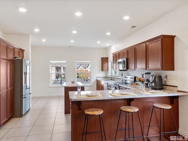 kitchen with light tile patterned floors, visible vents, a peninsula, stainless steel appliances, and a sink