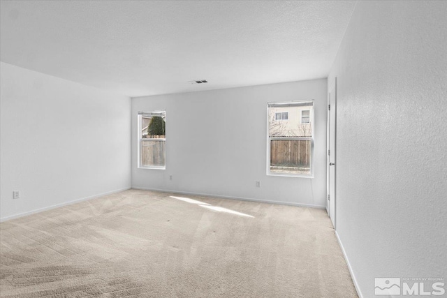 carpeted spare room featuring baseboards, a healthy amount of sunlight, visible vents, and a textured ceiling