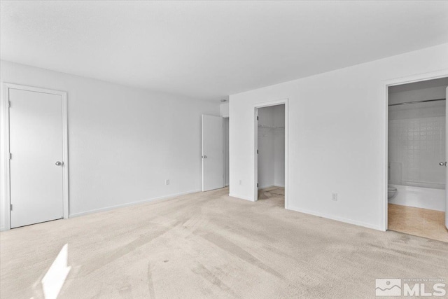 unfurnished bedroom featuring ensuite bath, carpet flooring, a walk in closet, and baseboards