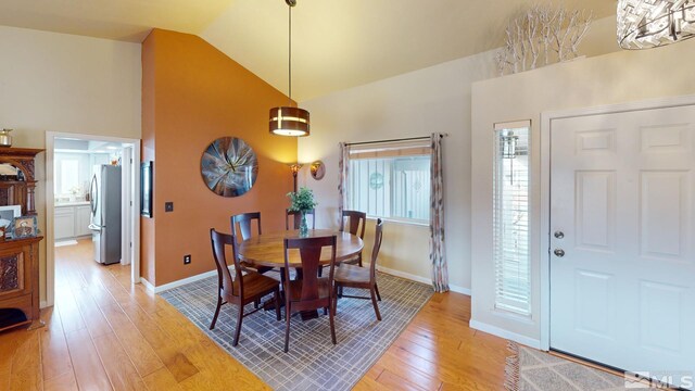 dining room with light wood-style floors, a healthy amount of sunlight, high vaulted ceiling, and baseboards