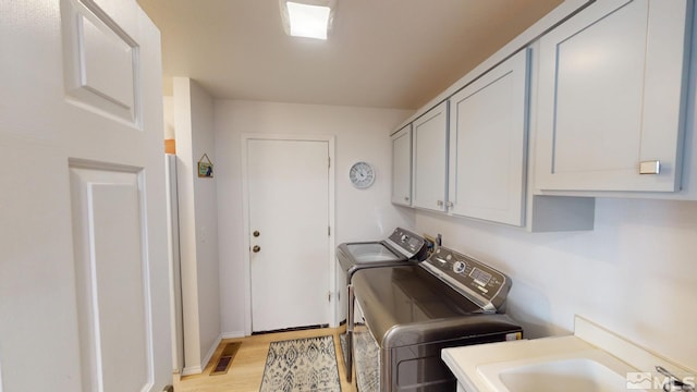 laundry room featuring washer and clothes dryer, visible vents, cabinet space, light wood-style flooring, and a sink