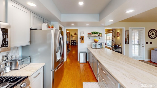 kitchen with light wood finished floors, decorative backsplash, a raised ceiling, light stone counters, and recessed lighting