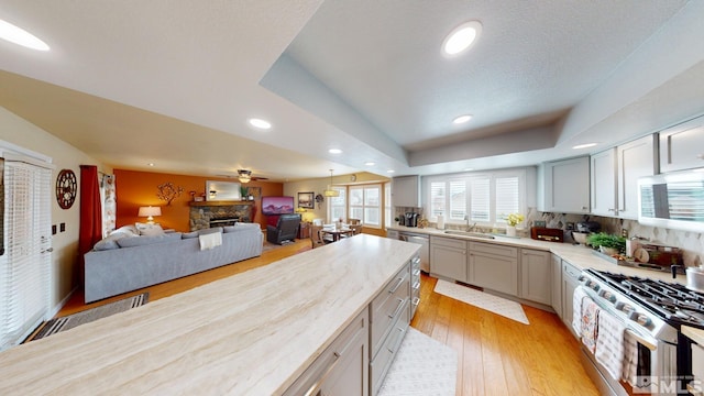 kitchen featuring a fireplace, stainless steel appliances, gray cabinetry, light wood-style floors, and a sink