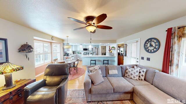 living area featuring light wood-type flooring, a textured ceiling, and a ceiling fan