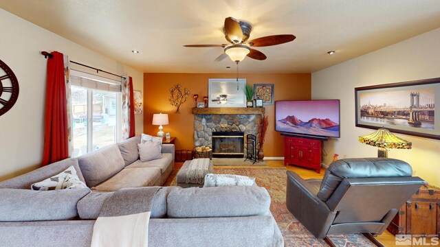 living area featuring a ceiling fan and a stone fireplace