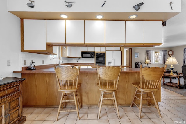 kitchen featuring light tile patterned floors, a peninsula, a sink, white cabinetry, and black appliances