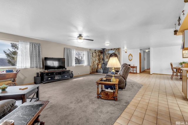 living room with a wood stove, light tile patterned flooring, ceiling fan, and baseboards