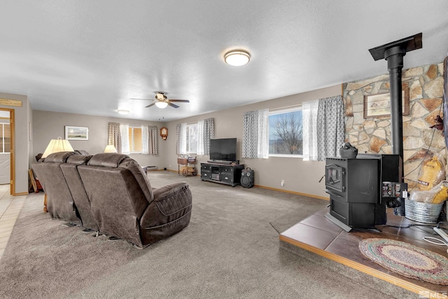 carpeted living area with ceiling fan, a wood stove, and baseboards