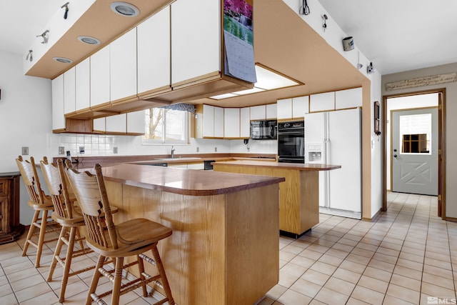 kitchen with a kitchen bar, a peninsula, black appliances, and tasteful backsplash