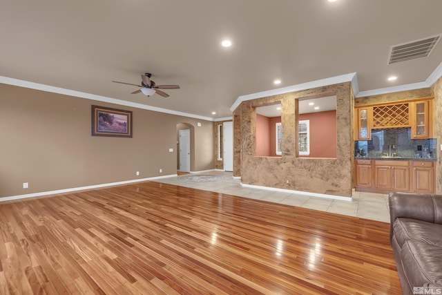 unfurnished living room featuring arched walkways, ceiling fan, a sink, visible vents, and light wood-style floors