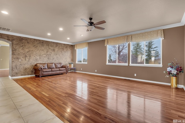 unfurnished living room with ornamental molding, arched walkways, visible vents, and plenty of natural light