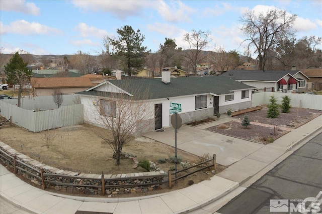 ranch-style house featuring fence private yard, stone siding, a chimney, and concrete driveway