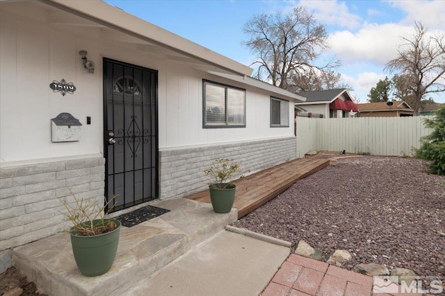 view of exterior entry featuring stone siding and fence