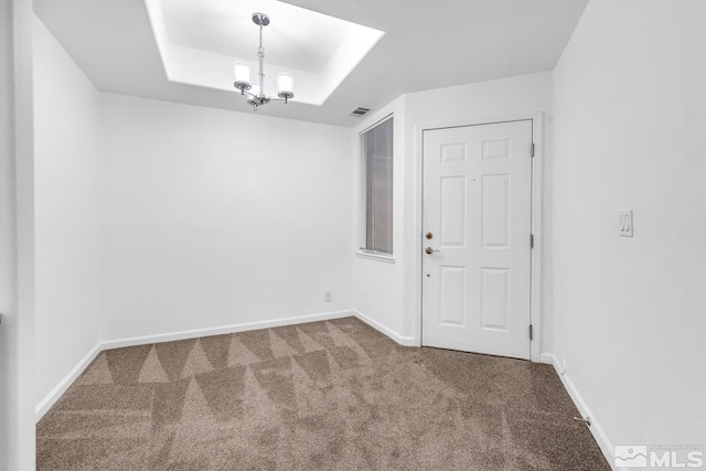 carpeted spare room featuring a notable chandelier, a tray ceiling, visible vents, and baseboards