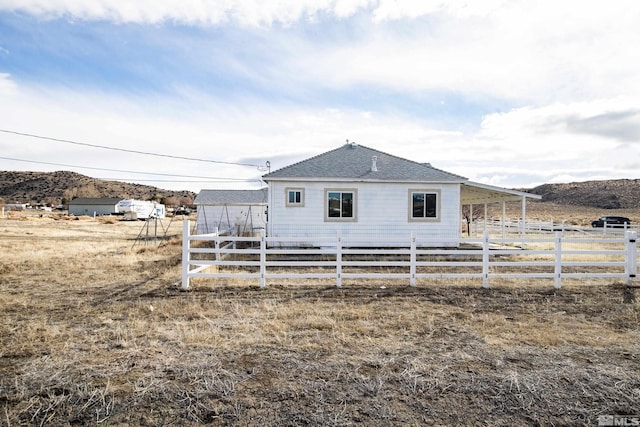 back of house with a shingled roof, a rural view, and fence