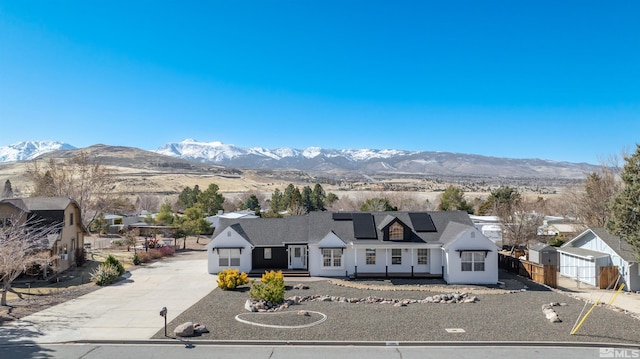 view of front of property featuring concrete driveway, fence, a mountain view, and roof mounted solar panels