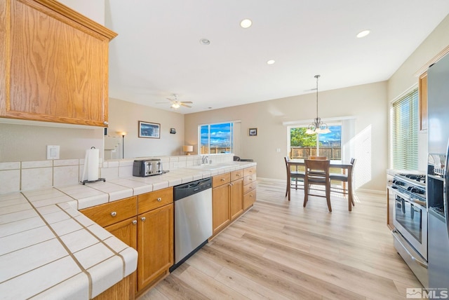 kitchen featuring a peninsula, light wood finished floors, tile countertops, and appliances with stainless steel finishes