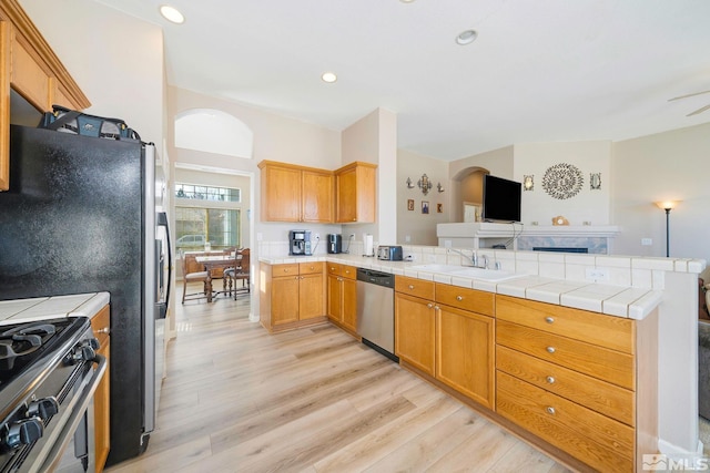 kitchen featuring open floor plan, a peninsula, stainless steel appliances, light wood-type flooring, and a sink