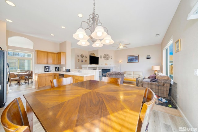 dining area with ceiling fan with notable chandelier, light wood-type flooring, a tile fireplace, and recessed lighting