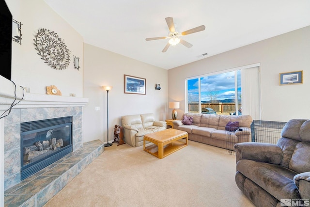 living room with ceiling fan, a tiled fireplace, visible vents, and carpet flooring