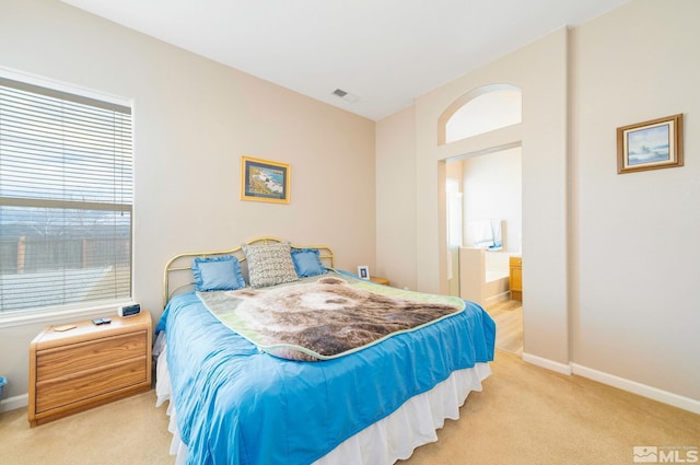 carpeted bedroom featuring ensuite bath, baseboards, and visible vents