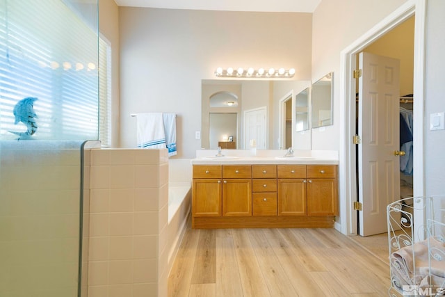 full bath with a tub, double vanity, a sink, and wood finished floors