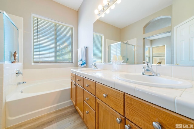 bathroom with a stall shower, a garden tub, a sink, and wood finished floors