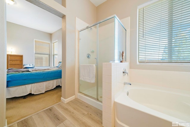 ensuite bathroom featuring a stall shower, connected bathroom, a bath, and wood finished floors