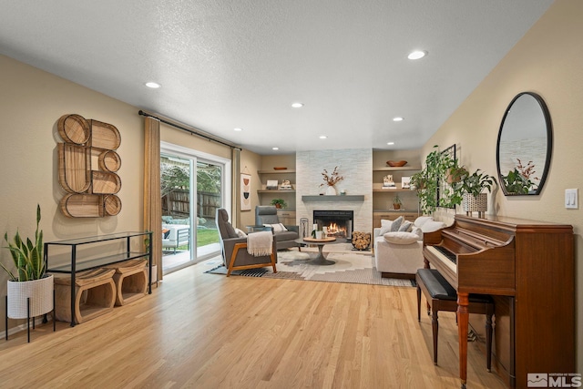 living room with built in shelves, a textured ceiling, light wood-style floors, a fireplace, and recessed lighting