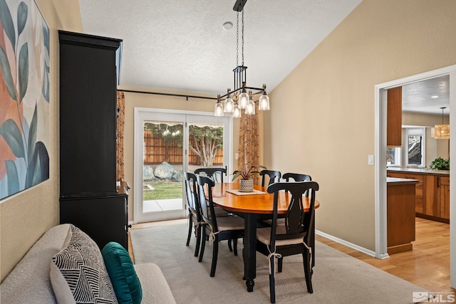 dining area featuring lofted ceiling, plenty of natural light, light wood-style flooring, and a textured ceiling