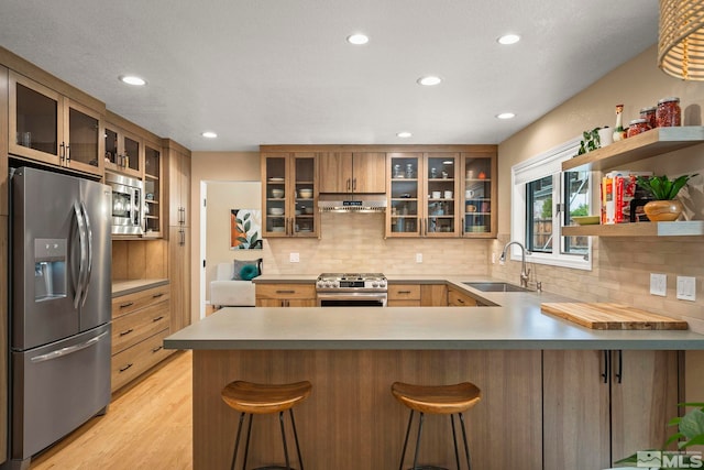 kitchen featuring appliances with stainless steel finishes, light wood-style floors, a sink, a peninsula, and under cabinet range hood