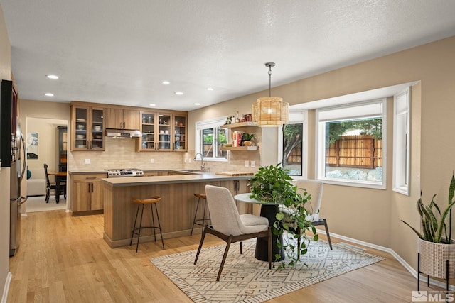 kitchen with under cabinet range hood, a peninsula, stove, a sink, and decorative backsplash