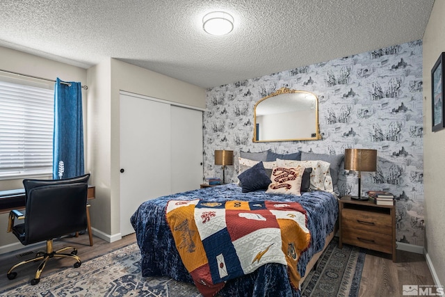 bedroom with baseboards, a closet, wood finished floors, and wallpapered walls