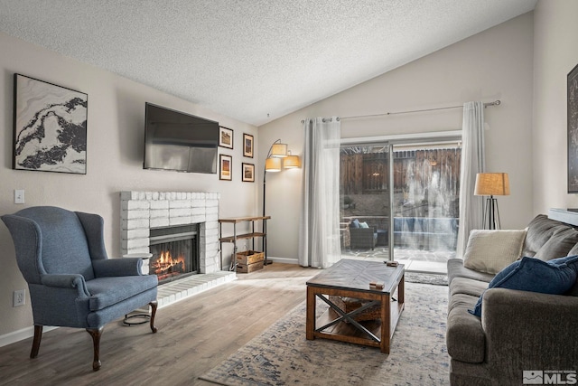 living area with a textured ceiling, a fireplace, wood finished floors, baseboards, and vaulted ceiling