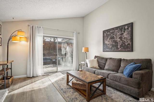 living area with vaulted ceiling, a textured ceiling, wood finished floors, and baseboards