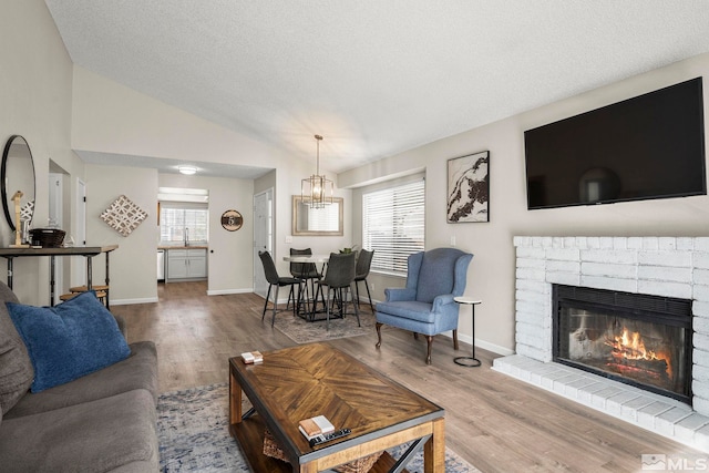 living room with a textured ceiling, a fireplace, wood finished floors, baseboards, and vaulted ceiling