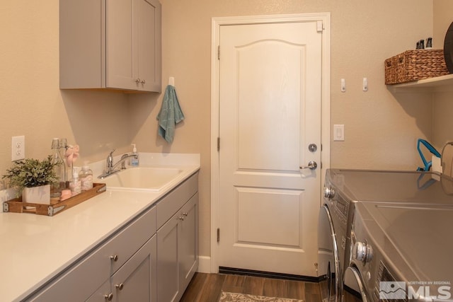 washroom with dark wood-type flooring, cabinet space, a sink, and washer and clothes dryer