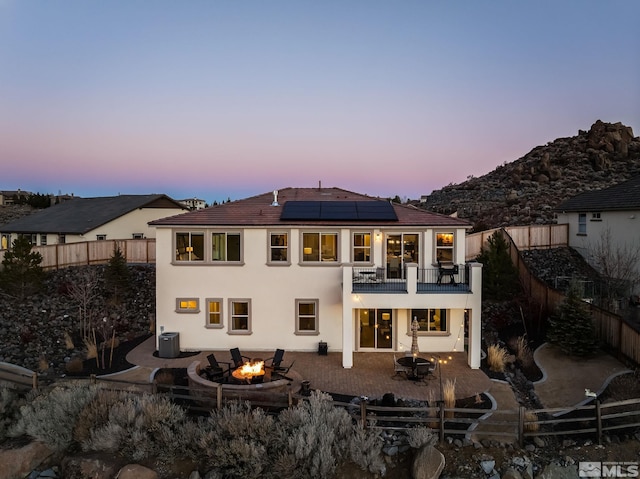 back of property at dusk featuring an outdoor fire pit, solar panels, a fenced backyard, a patio area, and stucco siding