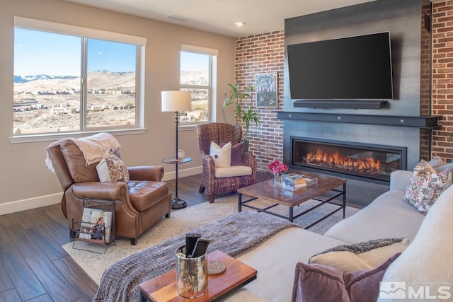 living room featuring a brick fireplace, baseboards, and wood finished floors