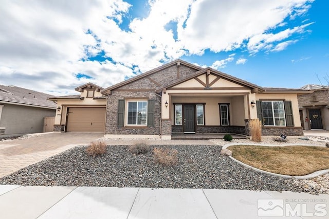 view of front of house featuring a garage, stone siding, decorative driveway, and stucco siding