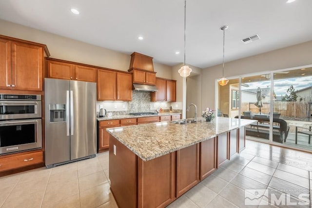 kitchen featuring visible vents, brown cabinetry, appliances with stainless steel finishes, under cabinet range hood, and a sink