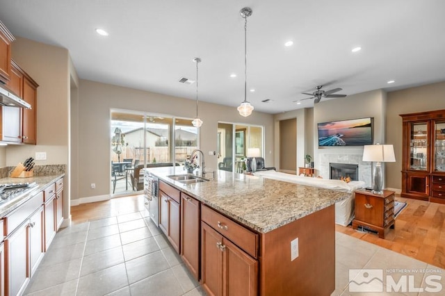 kitchen with light stone counters, a glass covered fireplace, brown cabinets, and a sink