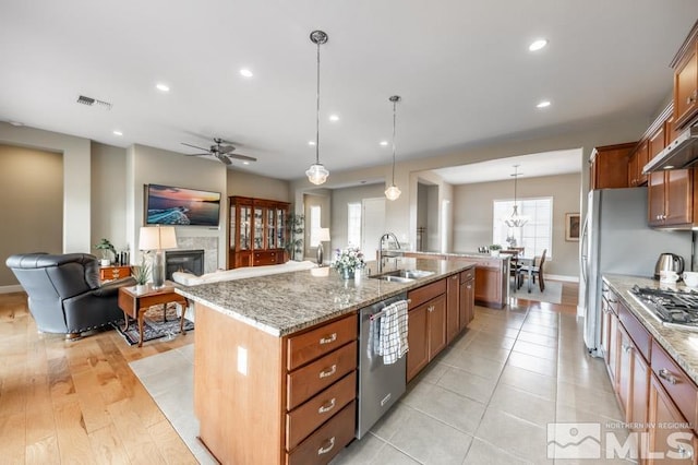 kitchen with visible vents, a glass covered fireplace, appliances with stainless steel finishes, light stone counters, and a sink