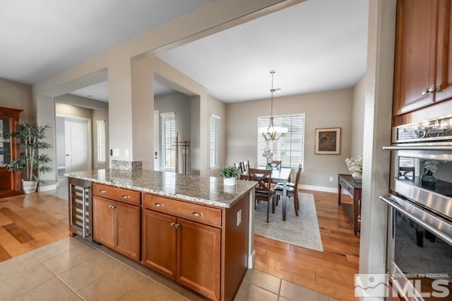 kitchen with stainless steel double oven, beverage cooler, a healthy amount of sunlight, light stone countertops, and brown cabinetry