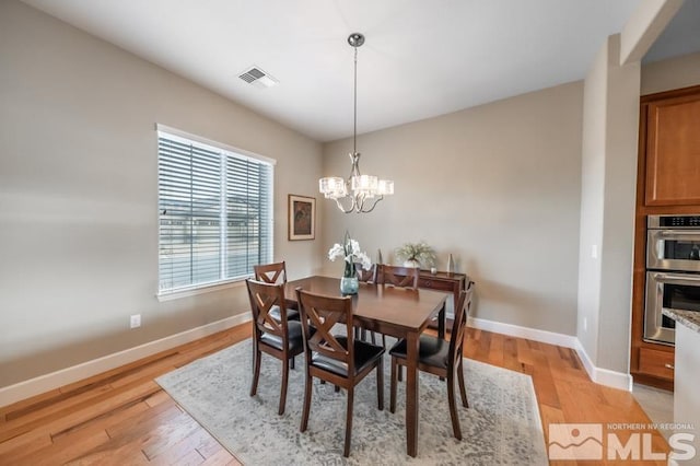 dining room with light wood finished floors, an inviting chandelier, visible vents, and baseboards