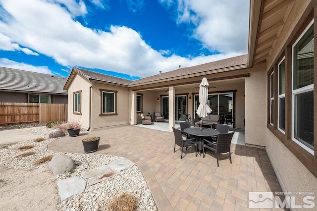 rear view of house with a patio, outdoor dining space, fence, and stucco siding